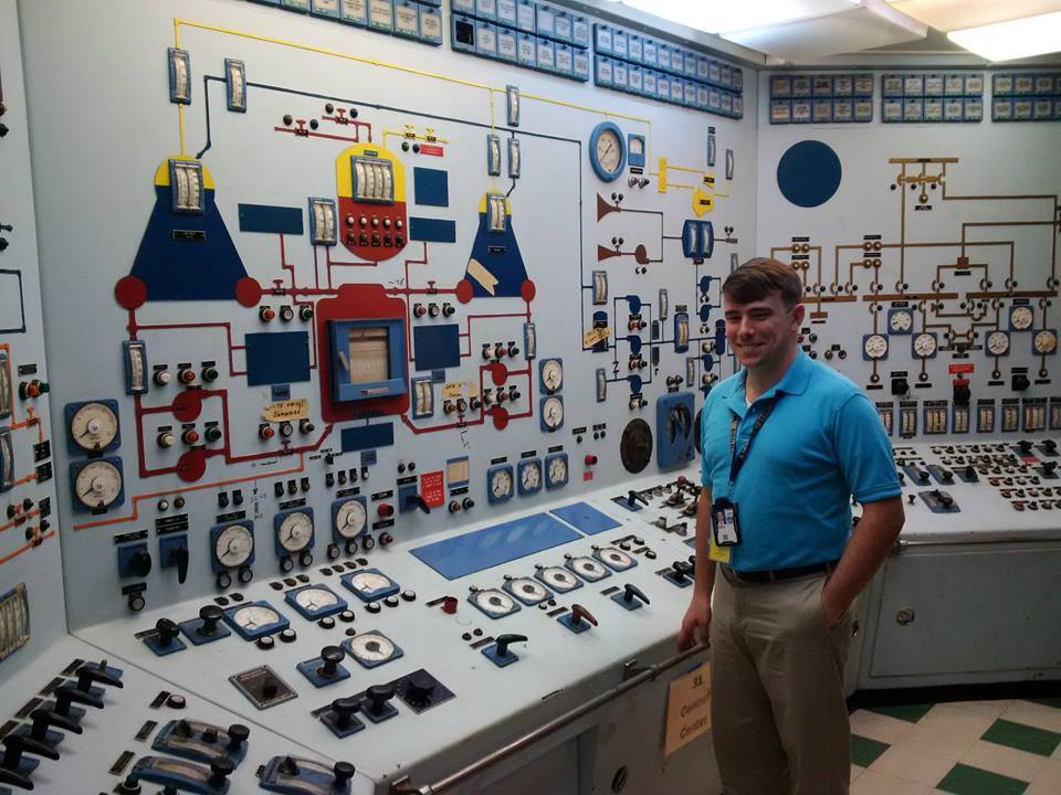 Michael Fitzgerald smiles while standing in front of the many buttons and dials that make up the control panel for the Nuclear Ship Savannah 